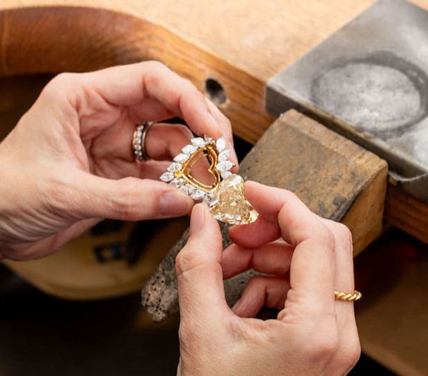 A woman is holding a heart shaped diamond and mount next to each other