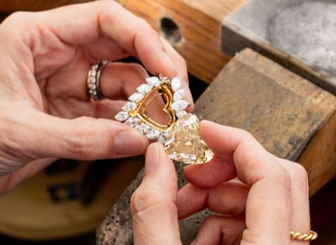 A woman is holding a heart shaped diamond and mount next to each other