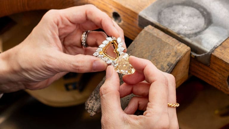 A woman is holding a heart shaped diamond and mount next to each other