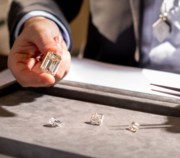A man is holding a large radiant shaped diamond with 3 other diamonds below