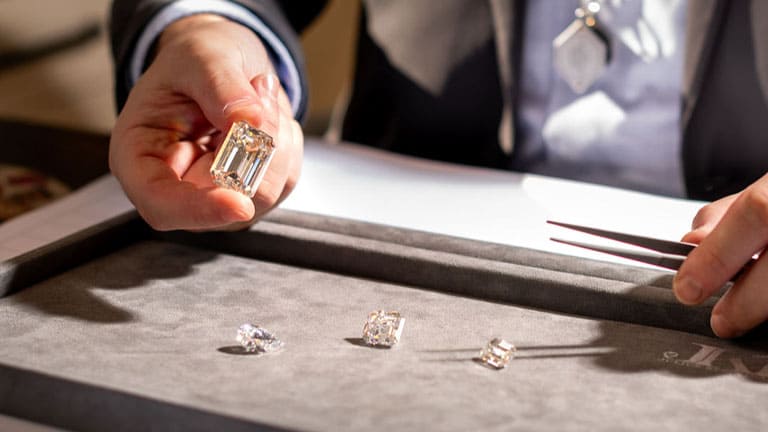 A man is holding a large radiant shaped diamond with 3 other diamonds below